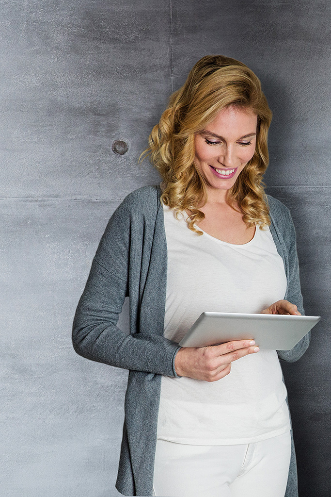 Symbolbild für Office Manager Jobs: Lächelnde schöne Frau vor grauer Wand mit Tablet